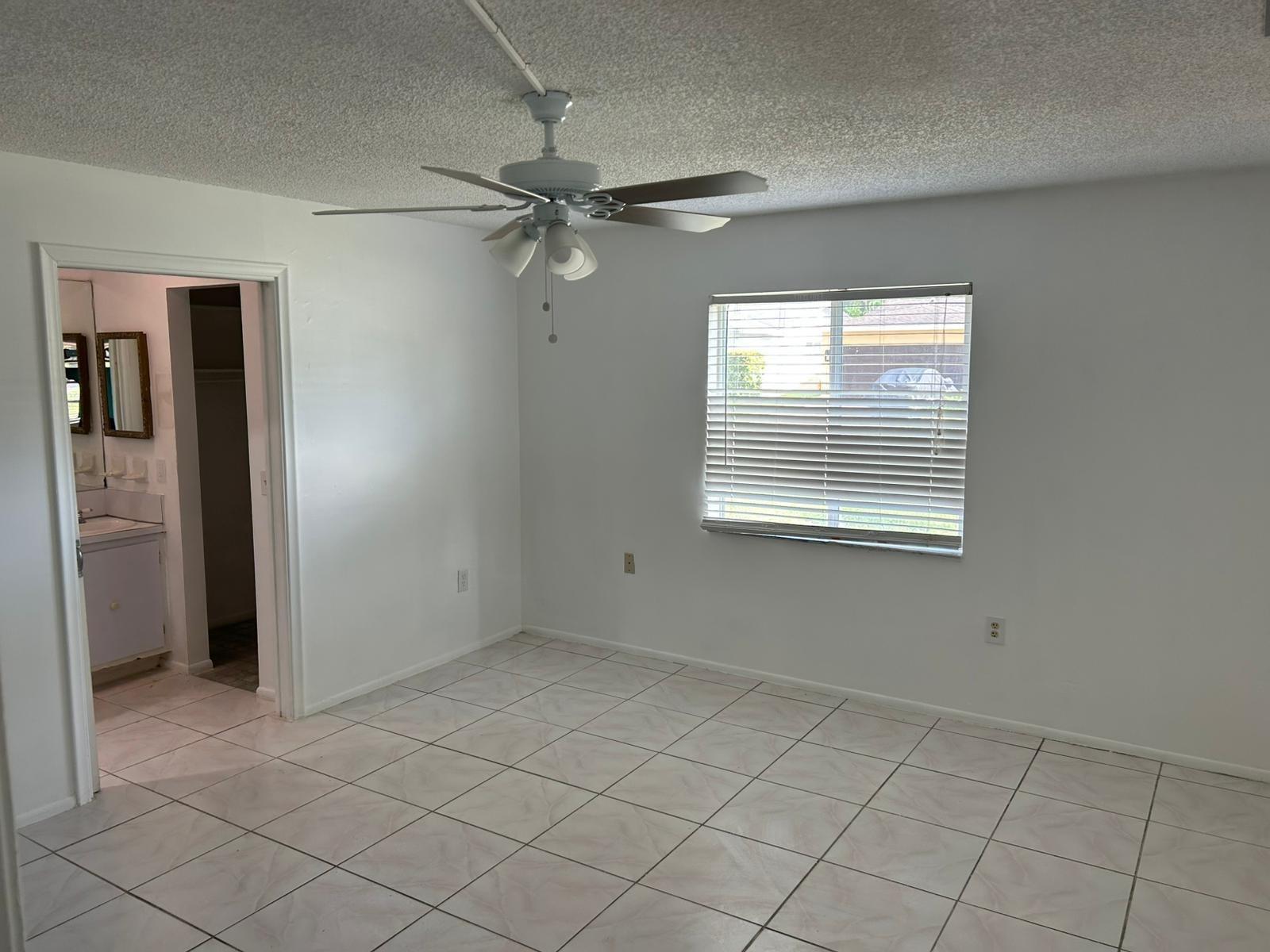 An empty bedroom with white walls, tile flooring, a ceiling fan, and an attached bathroom — 3405 Knolls Road, Miramar FL 33025, MIRAMAR, FL