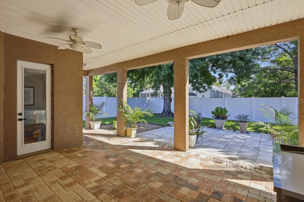 A covered patio features a brick floor, ceiling fans, and potted plants in a backyard — 58 BUTTERFIELD DRIVE, PALM COAST, FL