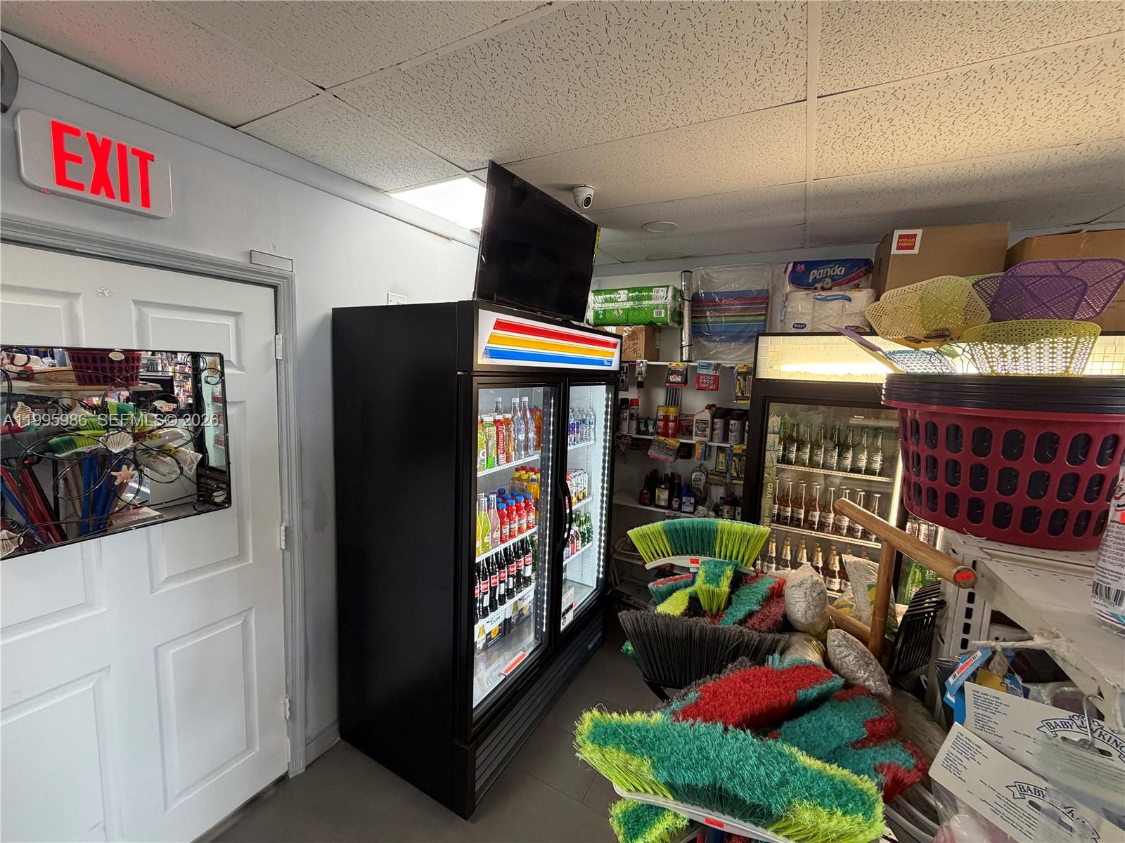A small retail space features two glass-door refrigerators, cleaning supplies, and an exit door — GROCERY STORE FOR SALE, Miami FL 33155, MIAMI, FL