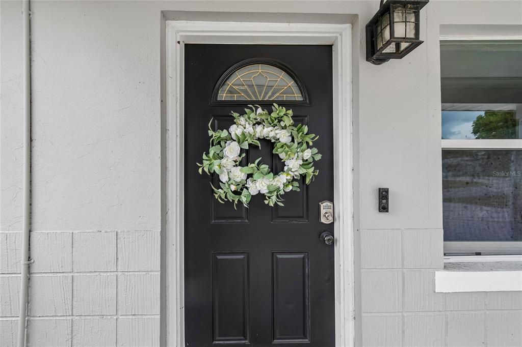 A black front door with a floral wreath is set in a light-colored exterior wall — 10746 109TH STREET, SEMINOLE, FL
