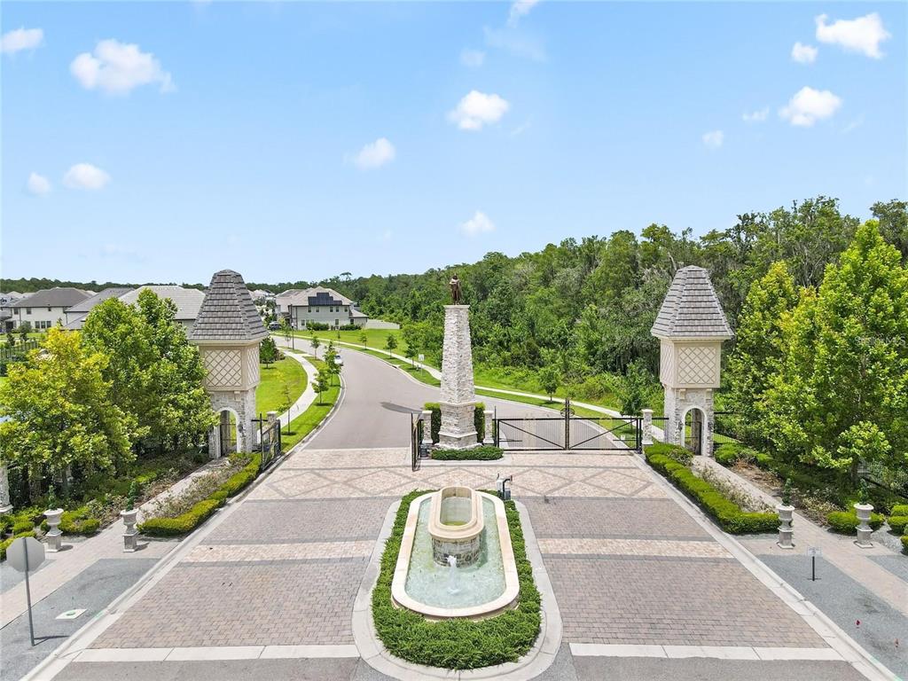 An aerial view shows a gated community entrance with stone pillars, a fountain, and landscaping — 10734 BELLE MAISONS DRIVE, ORLANDO, FL
