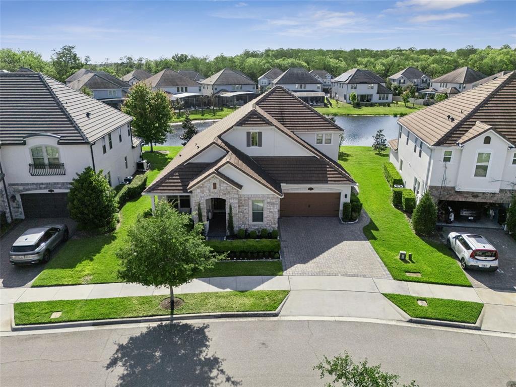 An aerial view shows a two-story suburban house with a tiled roof and stone facade — 10734 BELLE MAISONS DRIVE, ORLANDO, FL
