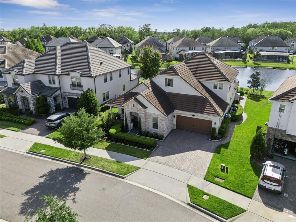 An aerial view shows two suburban houses with tile roofs, paved driveways, and a pond — 10734 BELLE MAISONS DRIVE, ORLANDO, FL