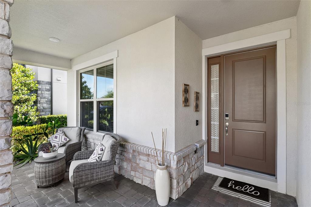 A covered front porch features stone accents, two wicker chairs, and a brown entry door — 10734 BELLE MAISONS DRIVE, ORLANDO, FL