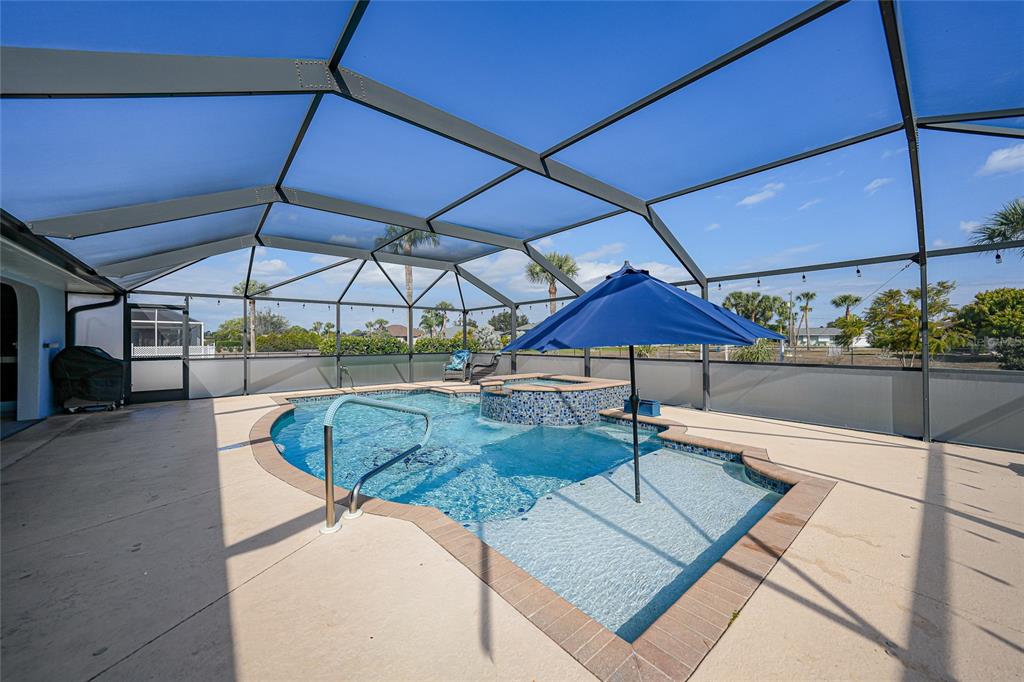 A screened-in patio features a swimming pool with an integrated hot tub and blue umbrella — 600 ROYAL POINCIANA, PUNTA GORDA, FL