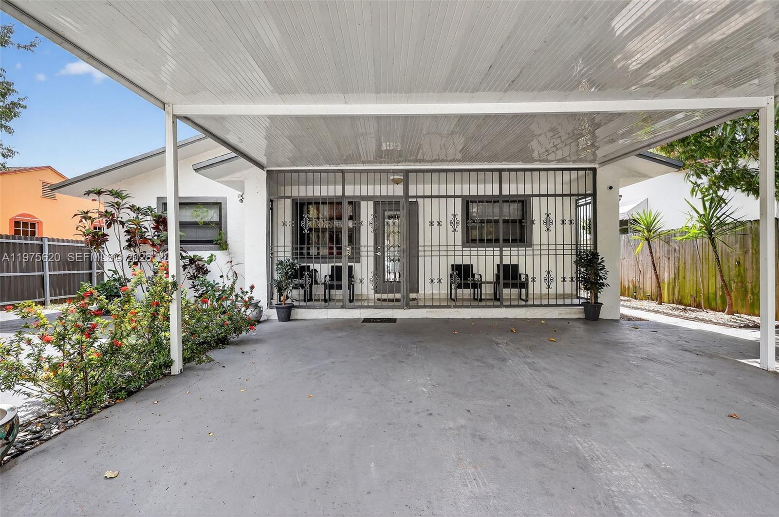 A covered concrete carport sits in front of a house with a gated entryway — 834 NW 115th St, Miami FL 33168, MIAMI, FL