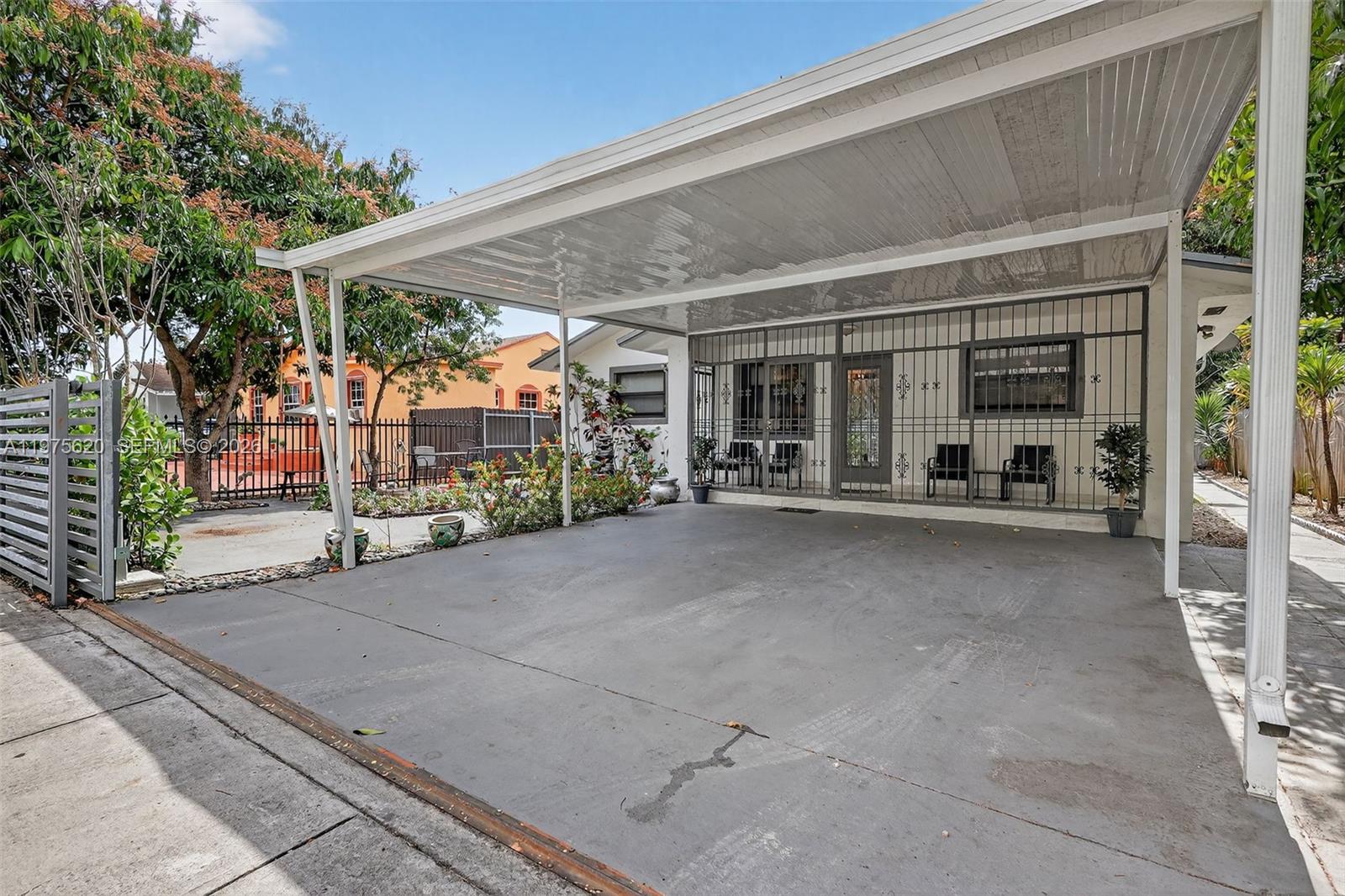 A concrete driveway with a metal carport leads to a house with security bars — 834 NW 115th St, Miami FL 33168, MIAMI, FL