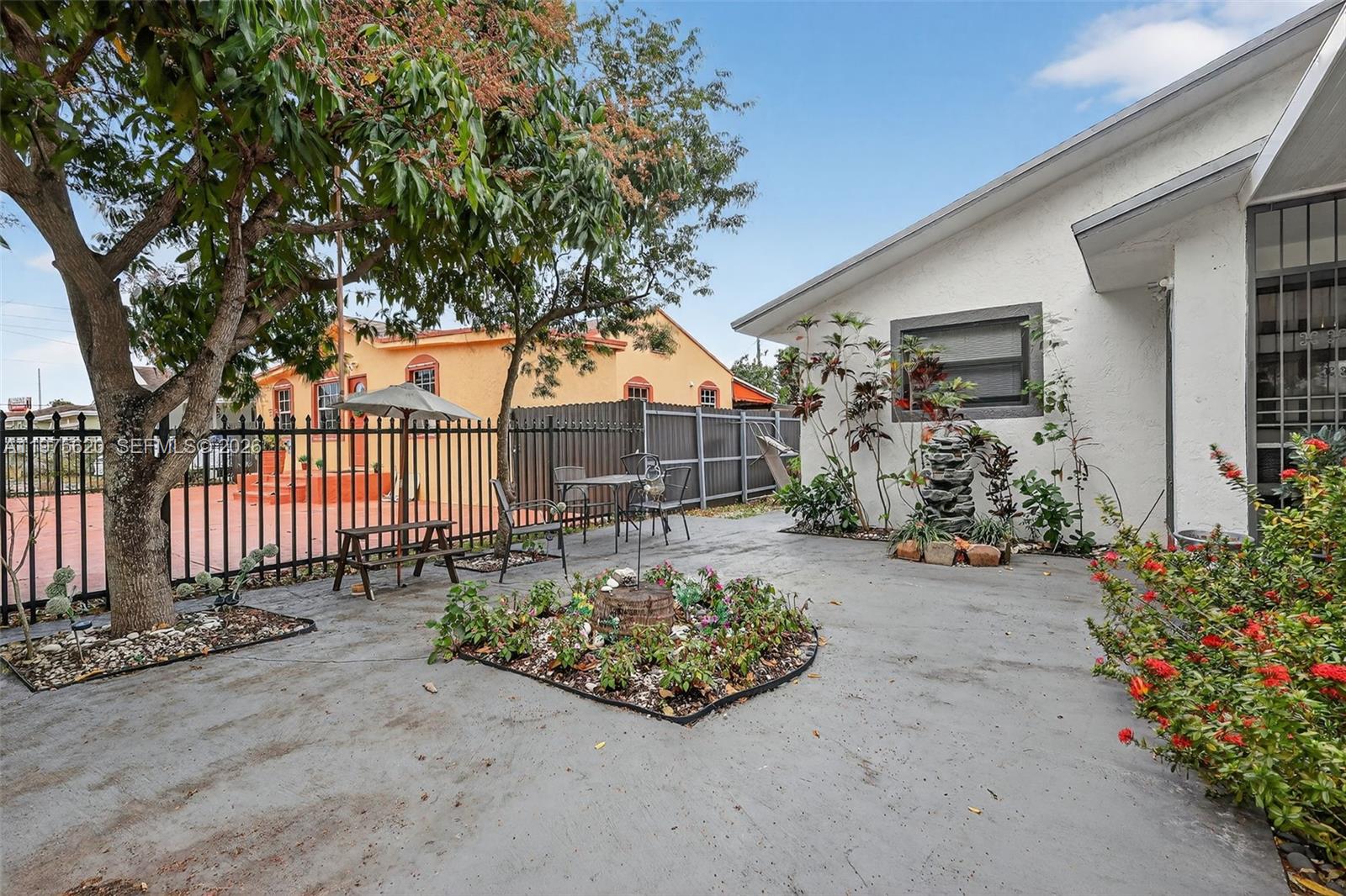 A paved backyard patio features a central garden bed, a small table, and metal fencing — 834 NW 115th St, Miami FL 33168, MIAMI, FL