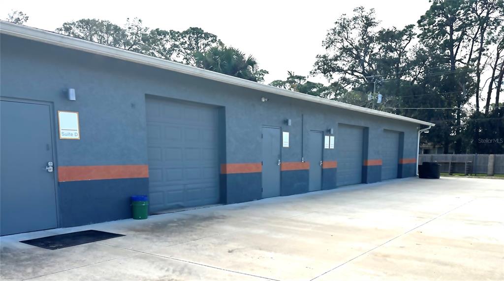 The exterior of a gray commercial building features multiple roll-up garage doors and entry doors — 2724 HIBISCUS DRIVE, EDGEWATER, FL
