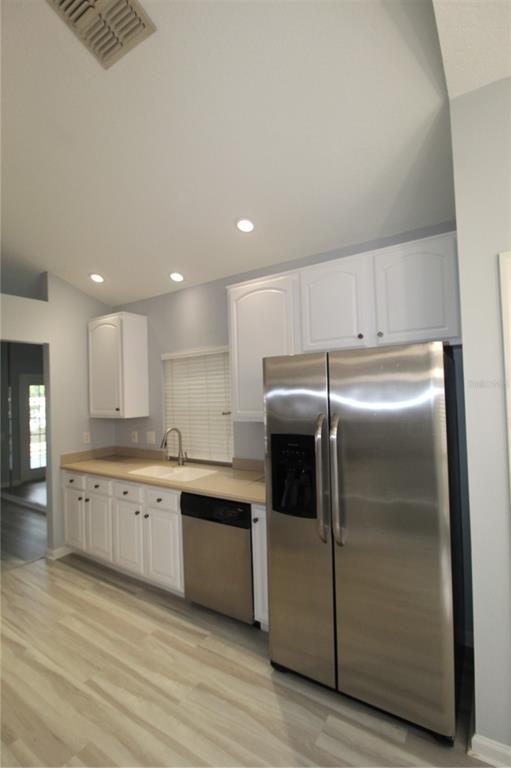 A kitchen features white cabinets, stainless steel appliances, a beige countertop, and light wood flooring — 6031 BAY VALLEY COURT, ORLANDO, FL