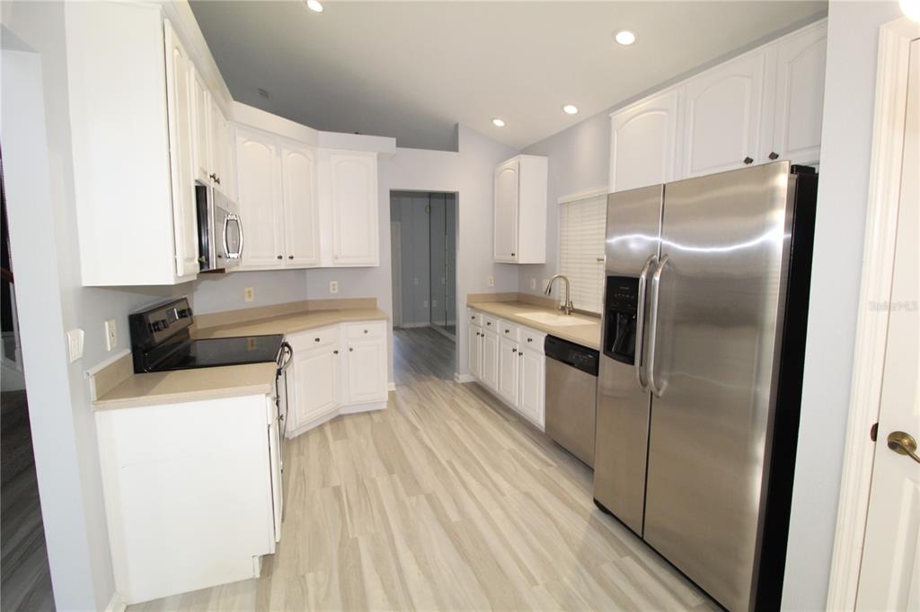 A kitchen features white cabinets, stainless steel appliances, tan countertops, and light wood-look flooring — 6031 BAY VALLEY COURT, ORLANDO, FL