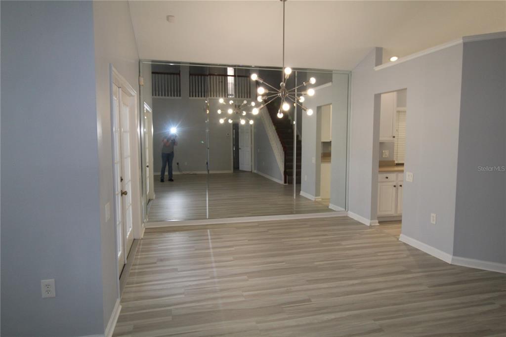 A room with light wood-look flooring, a large mirrored wall, and a modern chandelier — 6031 BAY VALLEY COURT, ORLANDO, FL
