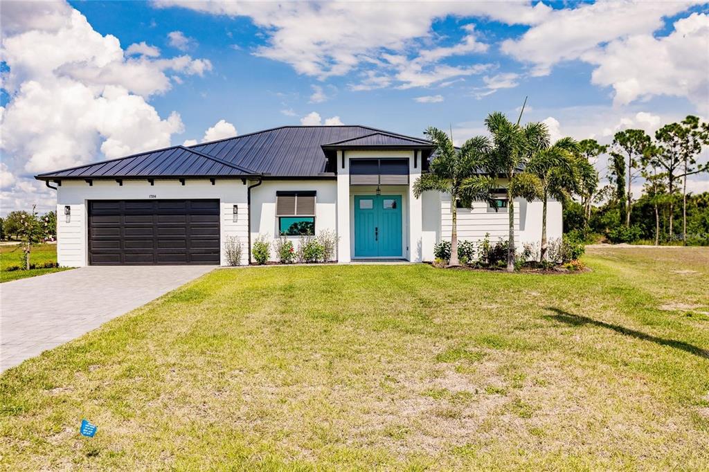 A single-story white house with a dark metal roof, black garage door, and teal door — 17512 CUILLAGAN COURT, PUNTA GORDA, FL