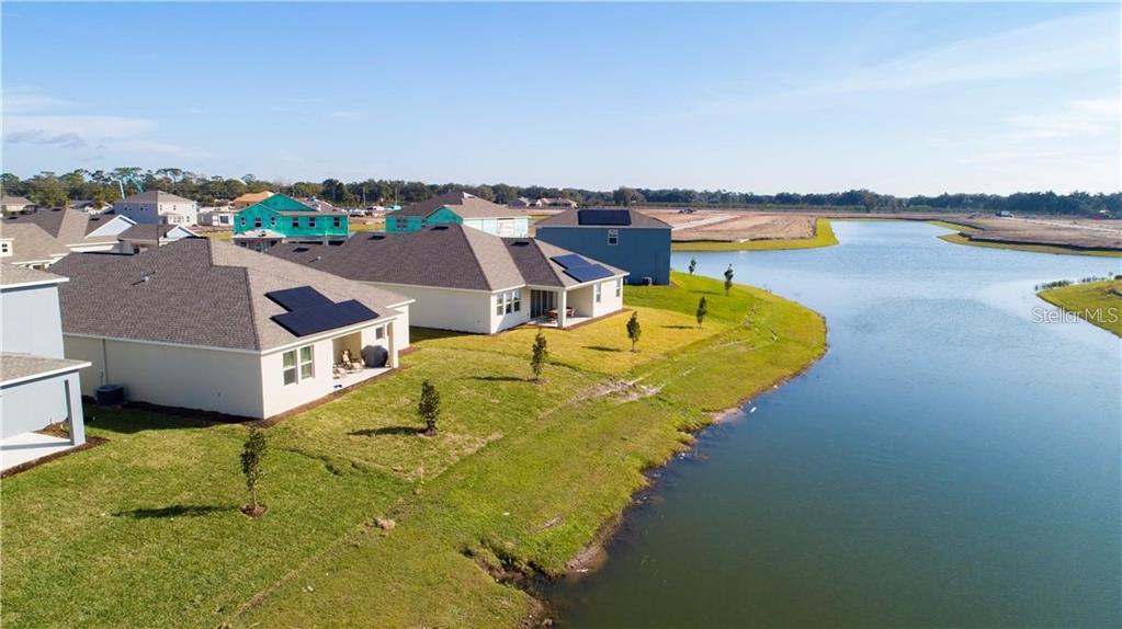 An aerial view shows several suburban houses with solar panels situated along a large pond — 4937 LOTTA COURT, ST CLOUD, FL