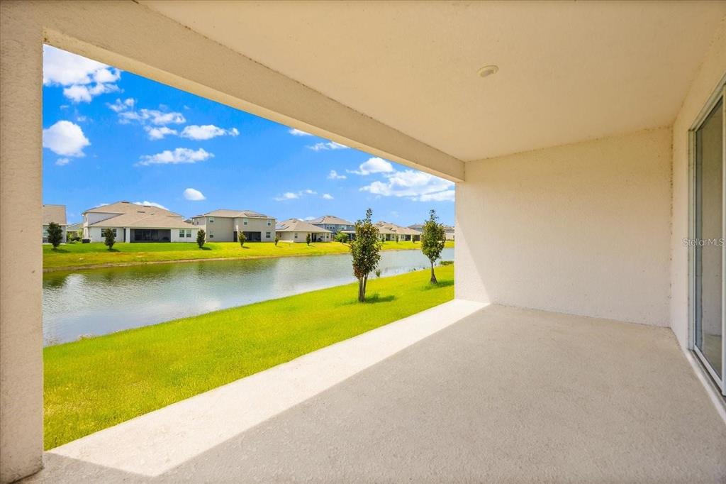 A covered concrete patio overlooks a grassy lawn, a small pond, and suburban houses — 4937 LOTTA COURT, ST CLOUD, FL
