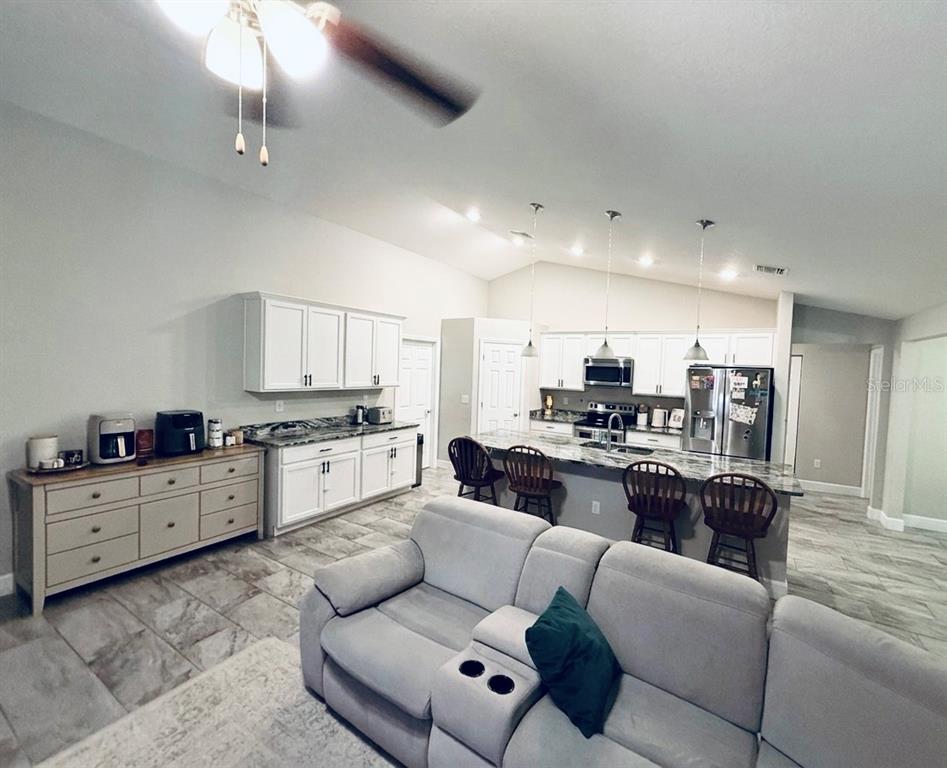 A kitchen with granite countertops overlooks a living room featuring a sectional sofa and fireplace — 5601 SW 117TH LANE ROAD, OCALA, FL