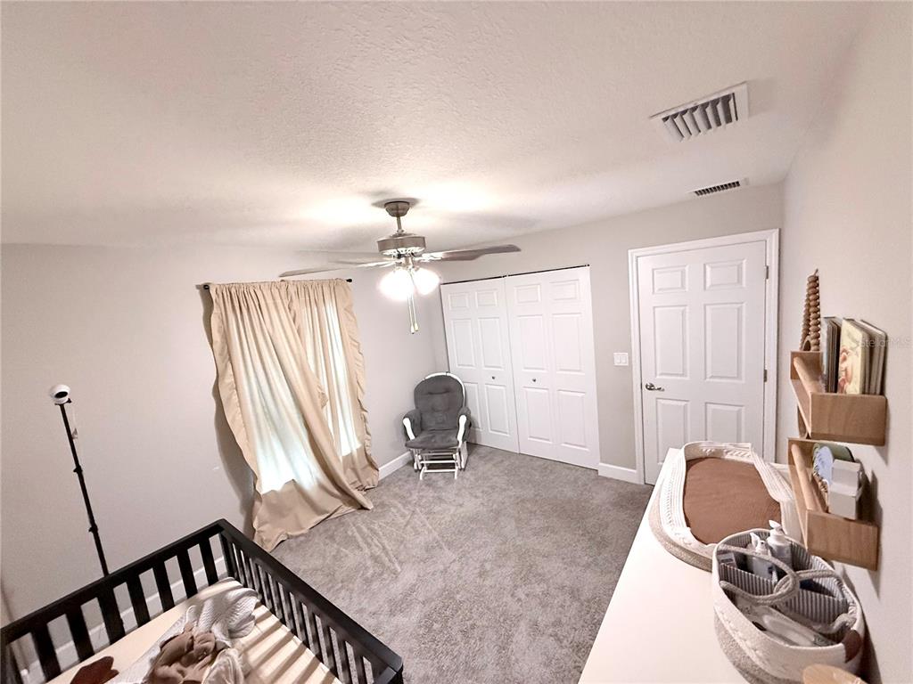 A bedroom features a tray ceiling, a bed with an orange comforter, and gray carpeting — 5601 SW 117TH LANE ROAD, OCALA, FL