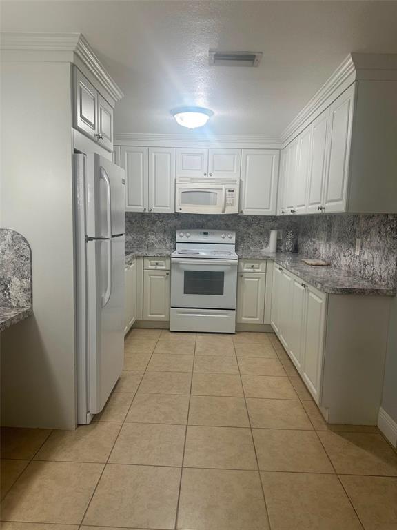 A kitchen features white cabinets, white appliances, and gray speckled countertops over tile flooring — 2106 AVALON ROAD, SEBRING, FL