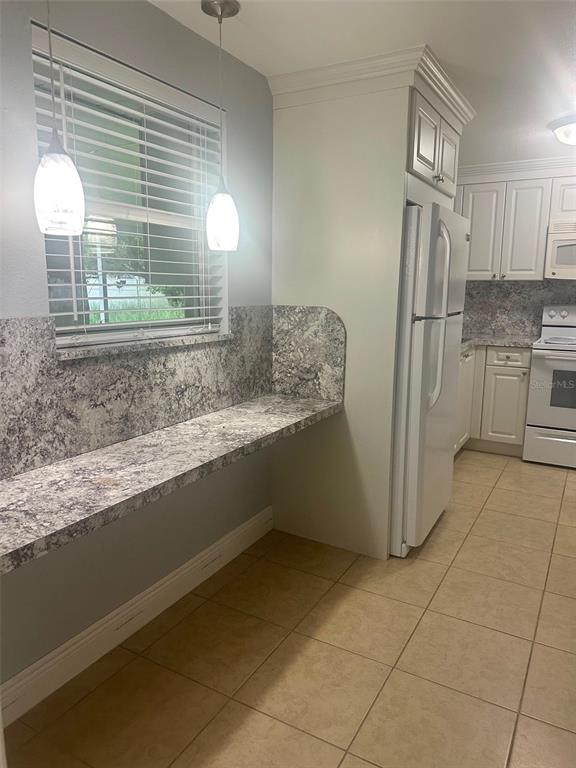 A kitchen features a long stone-look counter, white cabinets, a white refrigerator, and tile flooring — 2106 AVALON ROAD, SEBRING, FL