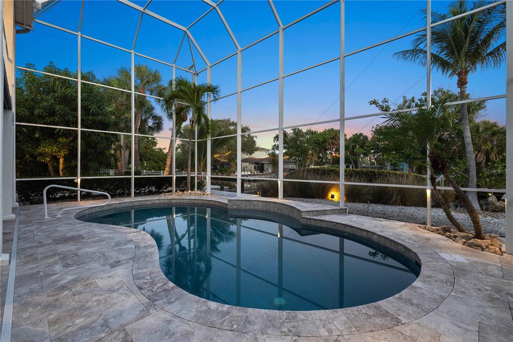 A screened-in pool area features a curved swimming pool surrounded by stone pavers at dusk — 412 TREASURE BOAT WAY, SARASOTA, FL