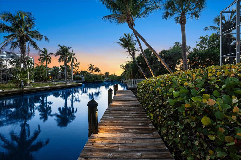 A wooden dock extends into a calm canal lined with palm trees at sunset — 412 TREASURE BOAT WAY, SARASOTA, FL