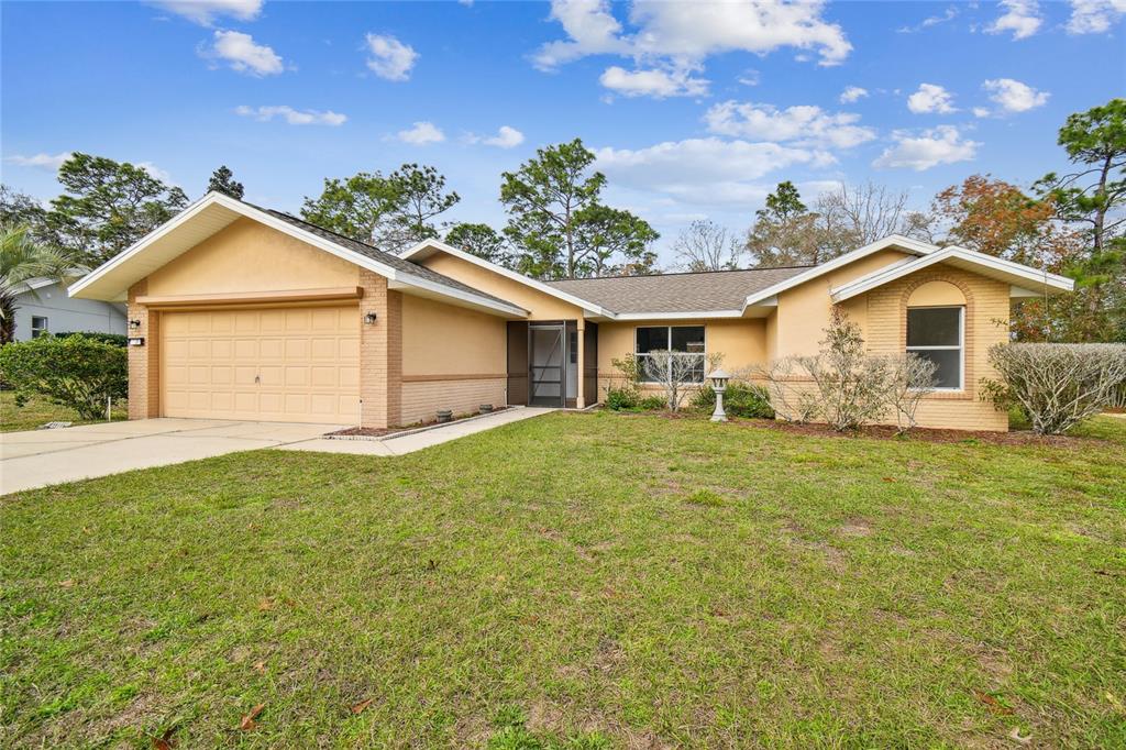 A single-story house with a tan stucco exterior, a two-car garage, and a front lawn — 11 CARNATION COURT E, HOMOSASSA, FL