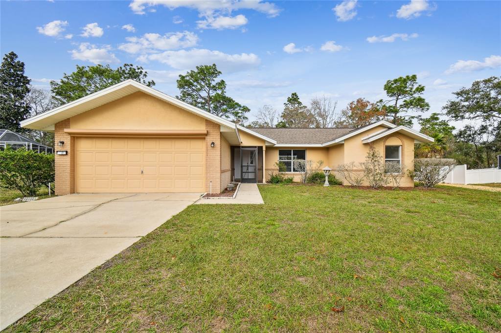 A single-story house with a tan stucco and brick exterior, a garage, and a lawn — 11 CARNATION COURT E, HOMOSASSA, FL