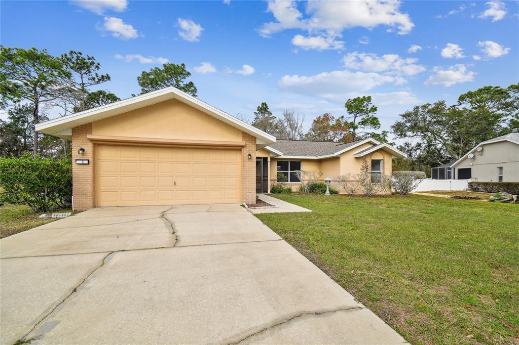 A single-story house with a tan exterior, a two-car garage, and a concrete driveway — 11 CARNATION COURT E, HOMOSASSA, FL