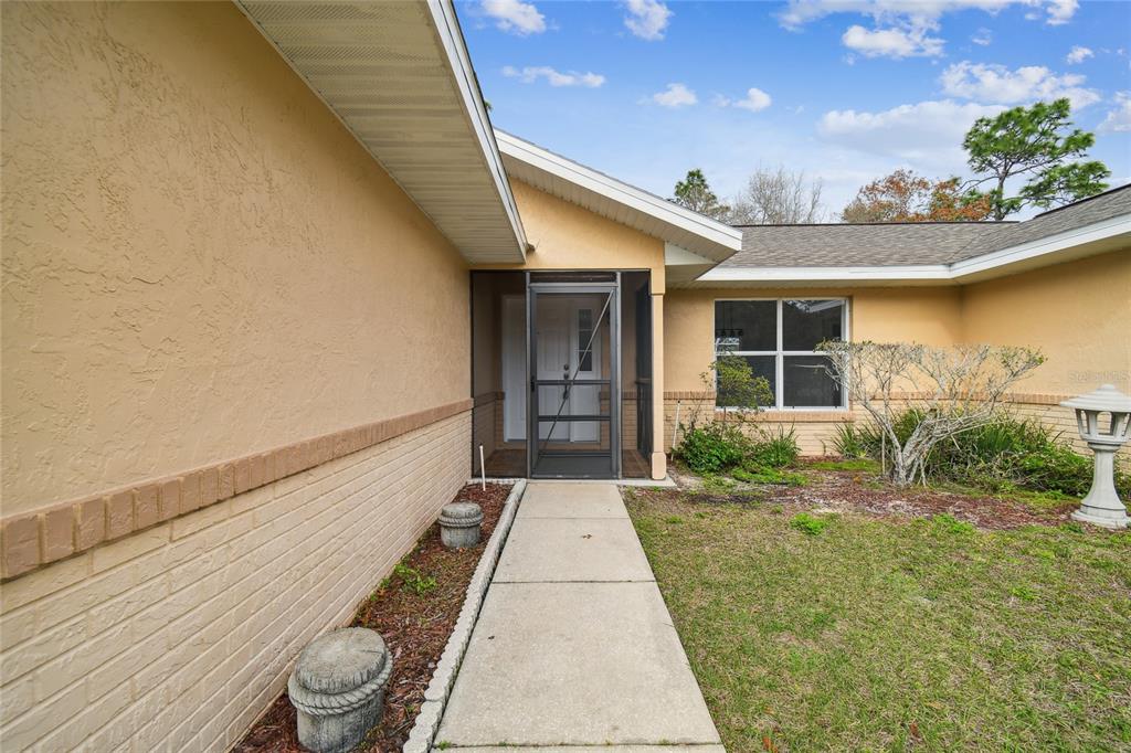 A concrete walkway leads to the screened front entryway of a tan stucco house — 11 CARNATION COURT E, HOMOSASSA, FL
