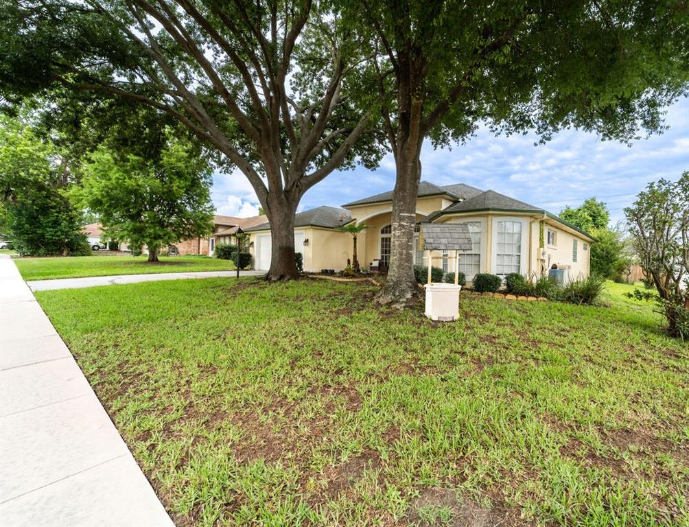 A single-story house with a beige exterior, a wishing well, and large trees in front — 107 NEEDLEWOOD LOOP, DEBARY, FL