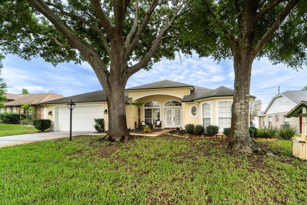 A yellow single-story house with a two-car garage and large trees in the front yard — 107 NEEDLEWOOD LOOP, DEBARY, FL