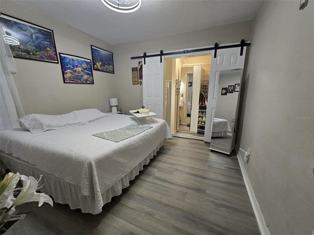 A bedroom features a large bed, light wood-look flooring, and sliding barn doors to a closet — 9320 N ELMER STREET, TAMPA, FL