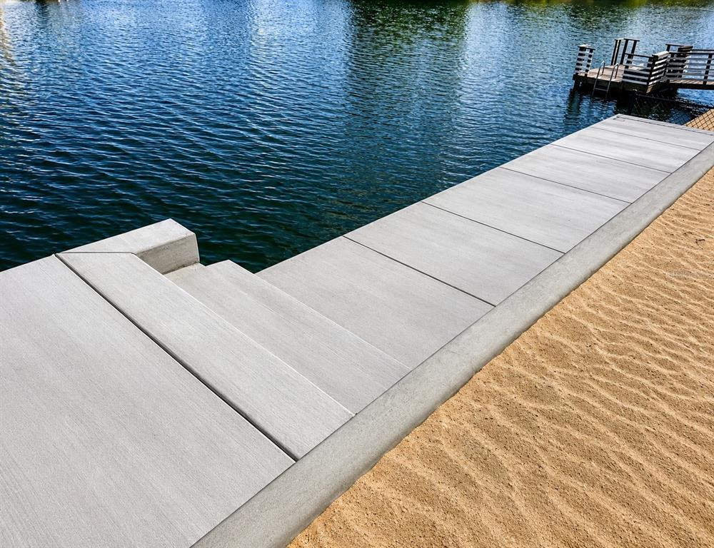 A concrete walkway with steps leads to a sandy beach beside a calm lake — 3511 AMBERJACK DRIVE, HERNANDO BEACH, FL