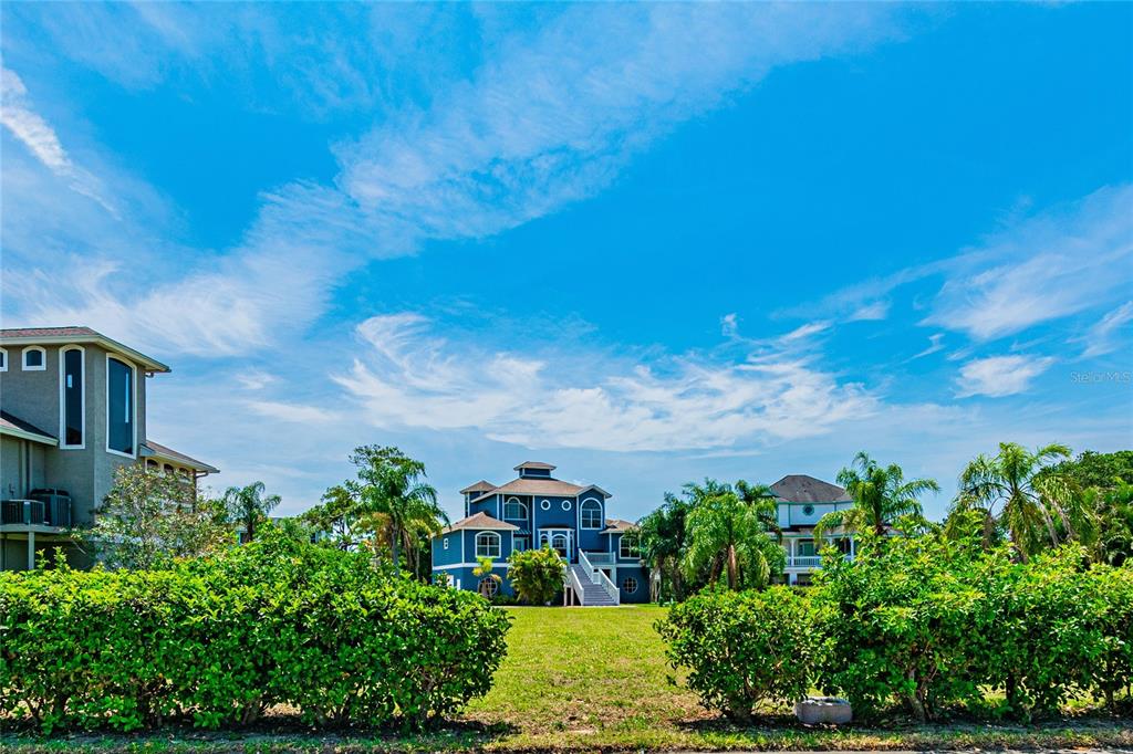 A blue multi-story house sits behind a green hedge under a bright blue sky — KETCH COURT, TARPON SPRINGS, FL