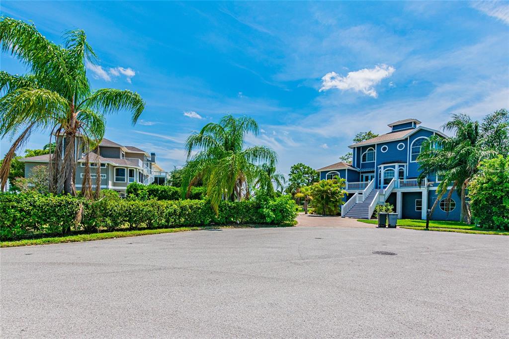 Two multi-story blue and grey houses stand behind a paved driveway with palm trees — KETCH COURT, TARPON SPRINGS, FL
