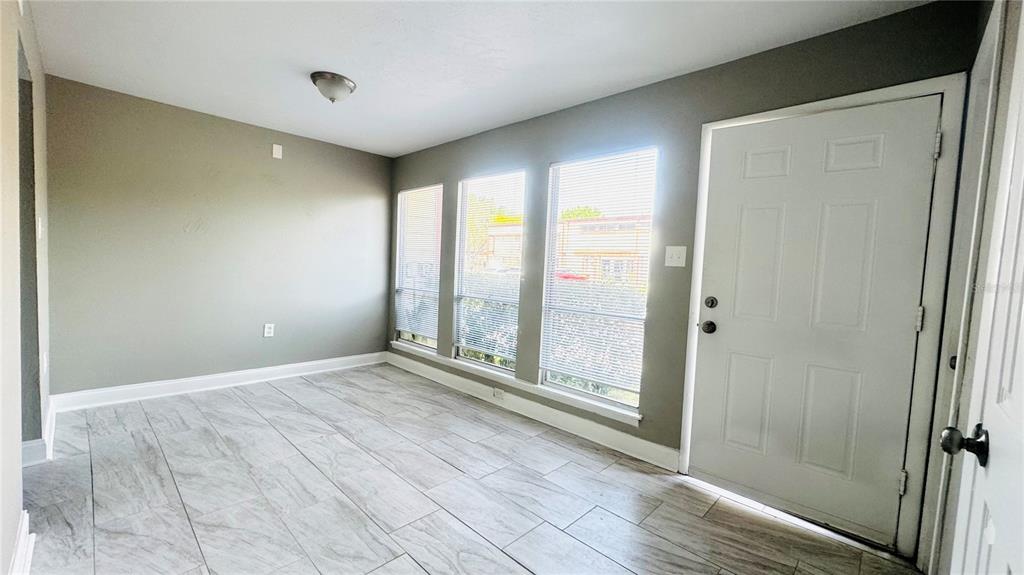 An empty room features gray walls, tile flooring, three windows with blinds, and a door — 4016 WOODFERN DRIVE UNIT B8, ORLANDO, FL