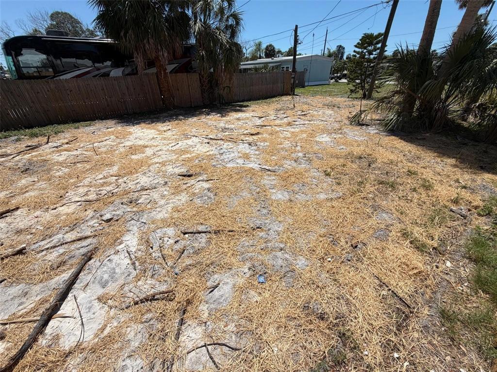 A sandy, sparsely vegetated outdoor lot features a wooden fence and several palm trees — 6825 GARDEN DRIVE, NEW PORT RICHEY, FL