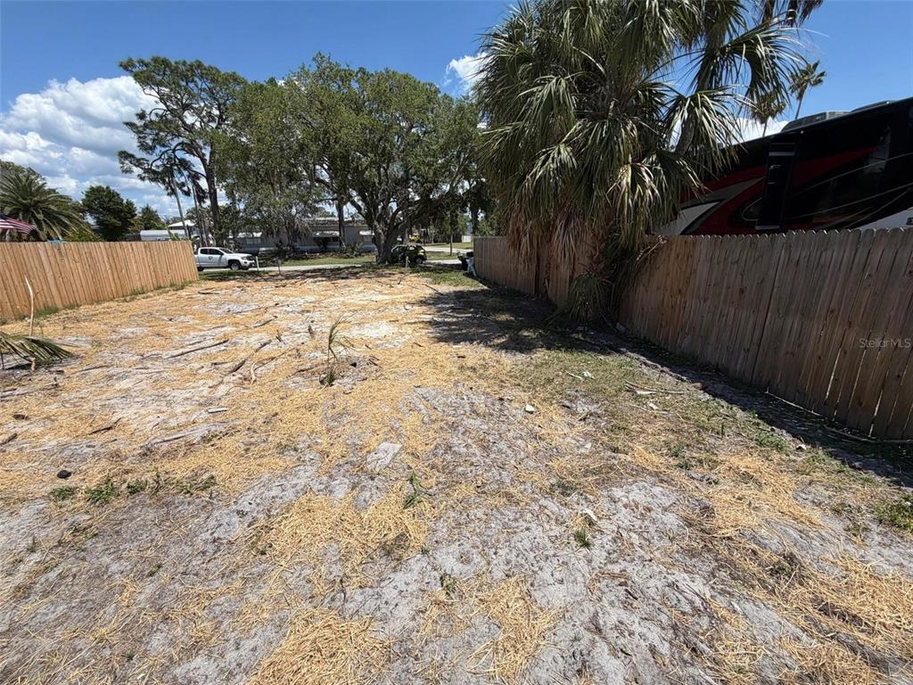 A vacant, sandy residential lot is enclosed by wooden fences with trees and a vehicle nearby — 6825 GARDEN DRIVE, NEW PORT RICHEY, FL
