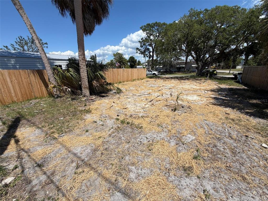 A vacant, sandy residential lot is enclosed by wooden fences with palm trees and foliage — 6825 GARDEN DRIVE, NEW PORT RICHEY, FL