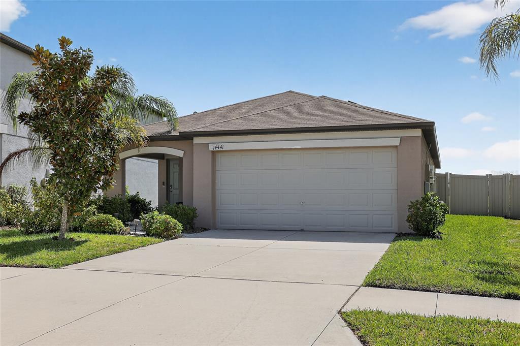 A single-story house with a beige stucco exterior, a two-car garage, and a front lawn — 14441 TOUCH GOLD LANE, SUN CITY CENTER, FL