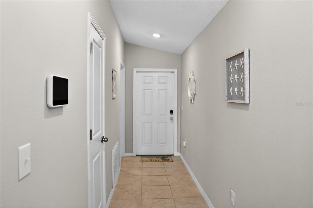 A tiled entryway features a white front door, a wall-mounted smart panel, and coastal decor — 14441 TOUCH GOLD LANE, SUN CITY CENTER, FL