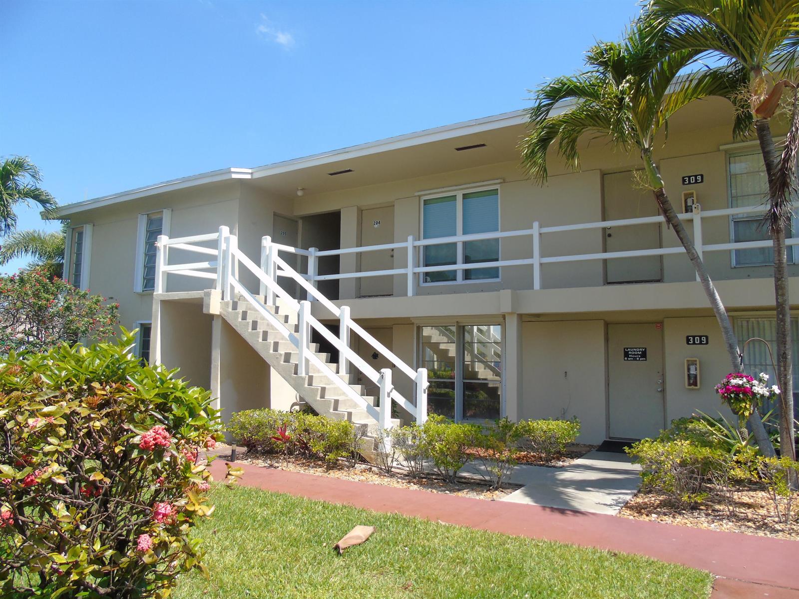 A two-story apartment building features an exterior staircase, white railings, and a ground-floor laundry room — 309 Circle Drive S # 204, Boynton Beach FL 33435, BOYNTON BEACH, FL