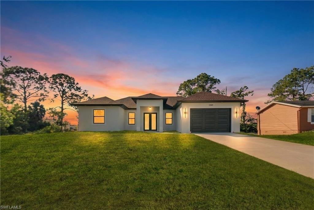 A modern single-story house with a gray exterior, dark garage door, and a grassy lawn — 2909 9th Street, Lehigh Acres FL 33971, LEHIGH ACRES, FL