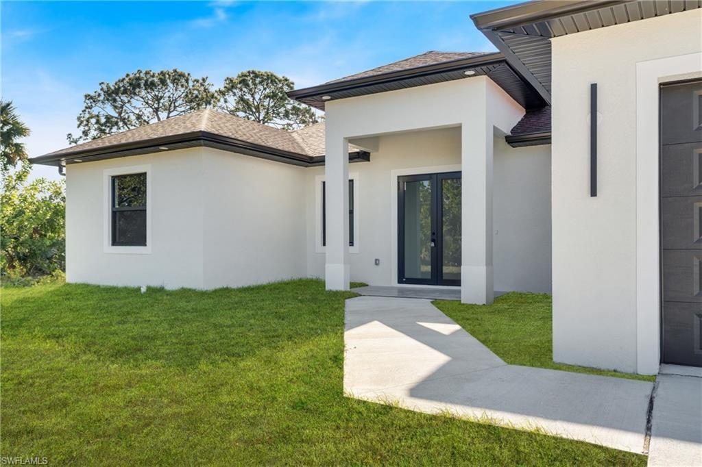 The exterior of a modern white house features a dark front door and garage door — 2909 9th Street, Lehigh Acres FL 33971, LEHIGH ACRES, FL