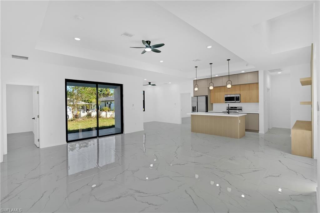 An open-concept living area features white marble-look tile floors, a kitchen island, and sliding glass doors — 2909 9th Street, Lehigh Acres FL 33971, LEHIGH ACRES, FL