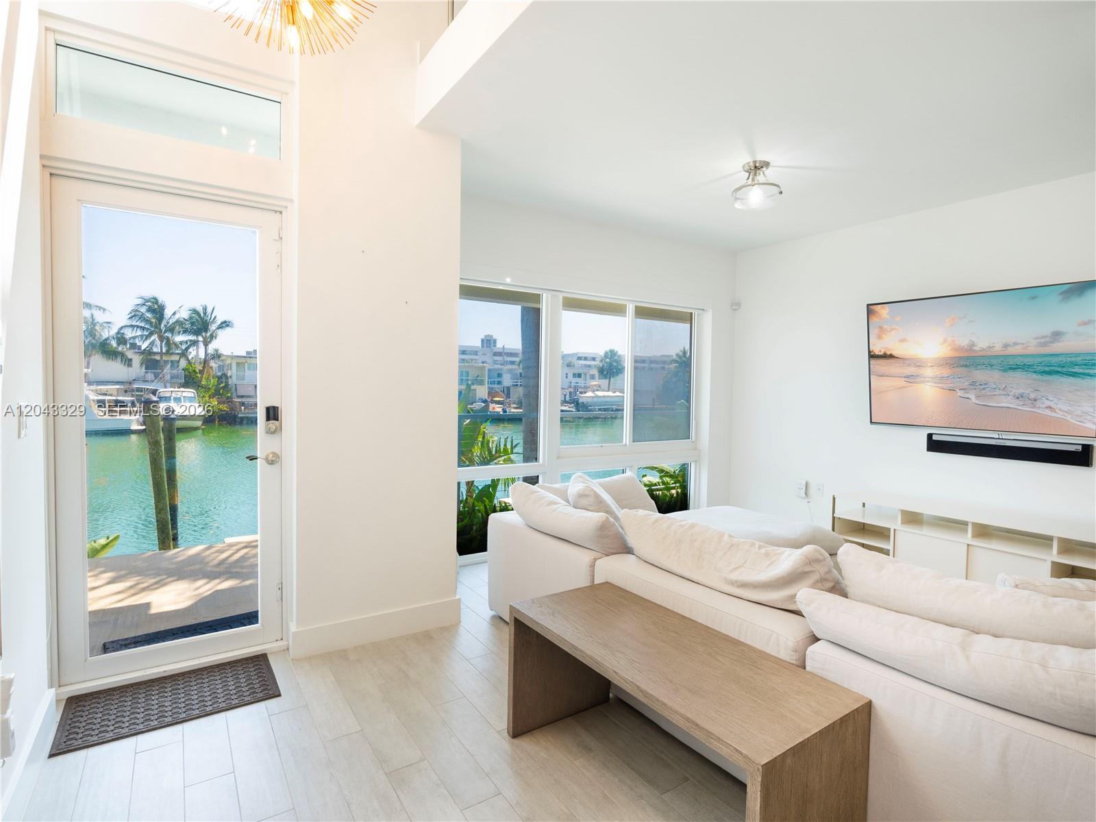 A bright living room features white sofas, a wooden bench, and a view of water — 51 N Shore Dr # 51, Miami Beach FL 33141, MIAMI BEACH, FL