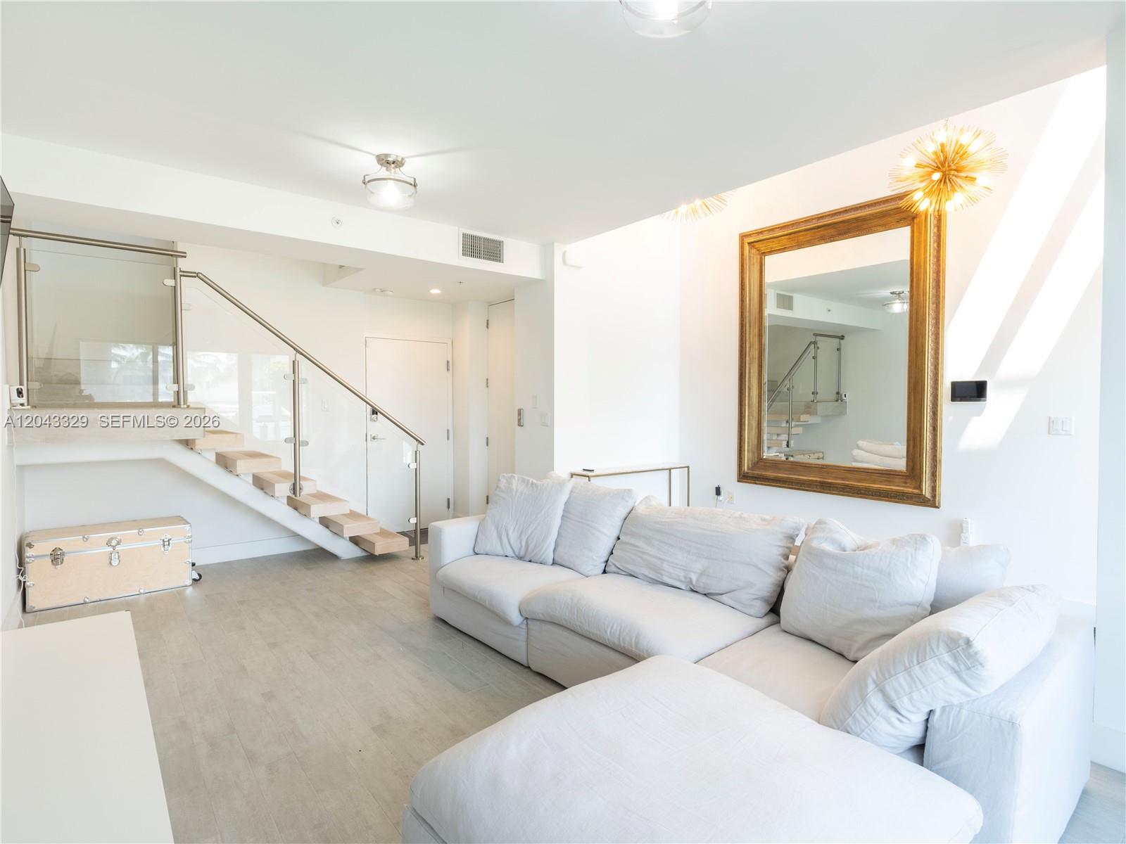 A living room features a white sectional sofa, a large gold-framed mirror, and floating stairs — 51 N Shore Dr # 51, Miami Beach FL 33141, MIAMI BEACH, FL