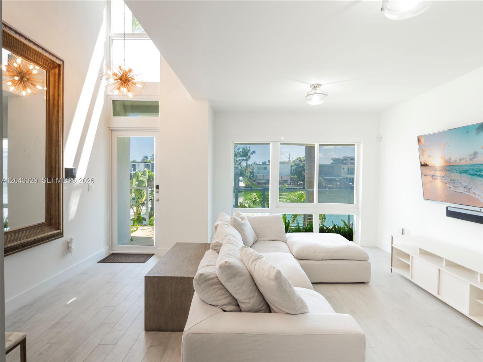 A bright living room features a white sectional sofa, a large mirror, and waterfront views — 51 N Shore Dr # 51, Miami Beach FL 33141, MIAMI BEACH, FL