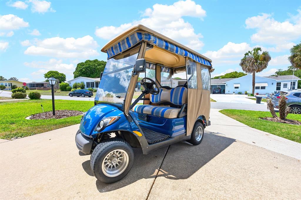 A blue golf cart with a striped canopy sits on a concrete driveway — 1603 COG HILL DRIVE, LADY LAKE, FL