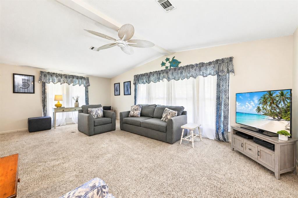 A living room features a gray sofa, matching armchair, carpeted floors, and a television console — 1603 COG HILL DRIVE, LADY LAKE, FL